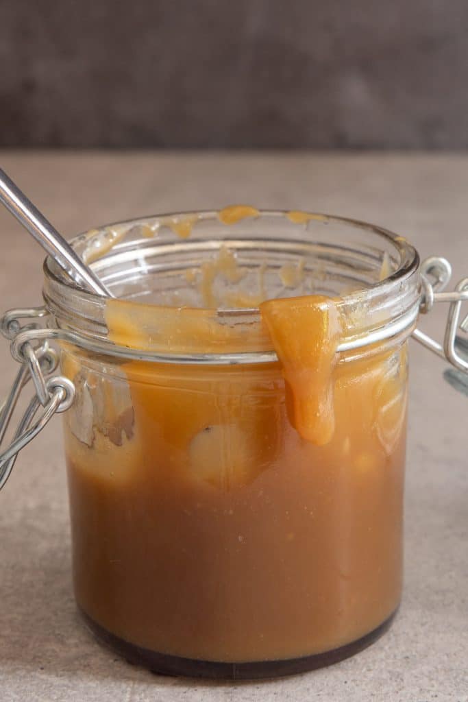 Caramel sauce in a glass jar with spoon inside.