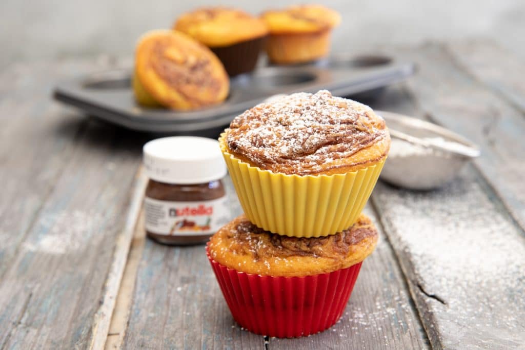 muffins with powder sugar on top and a small jar of nutella in the back.