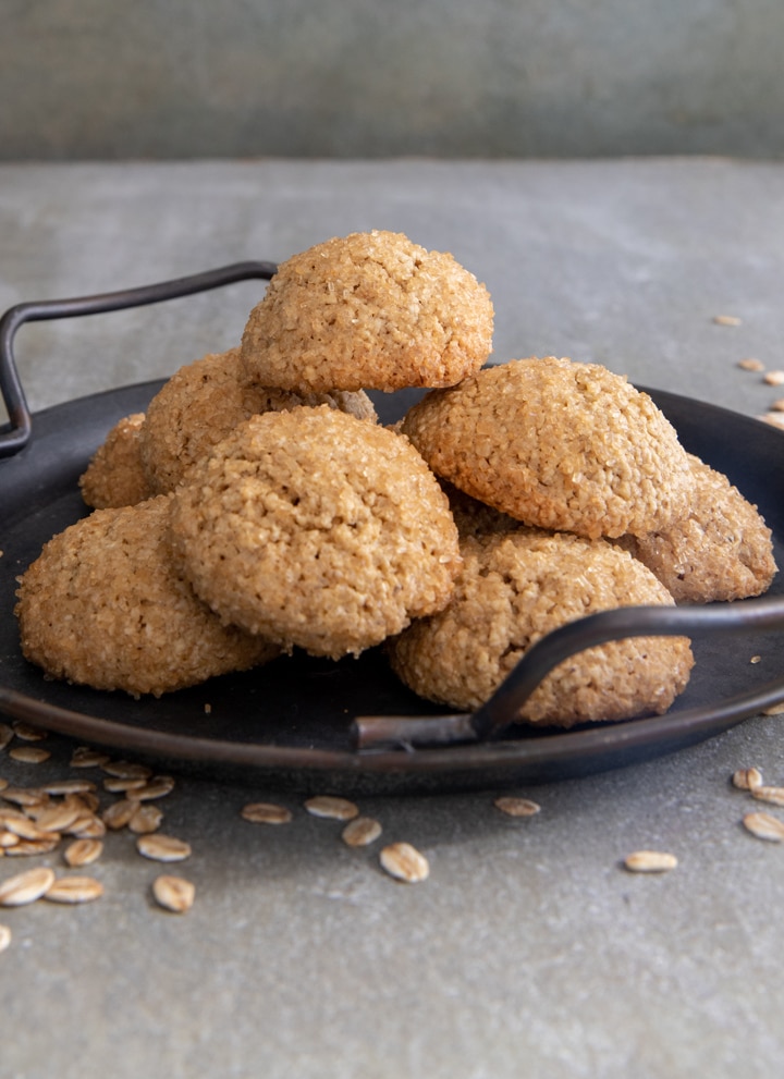 Cookies on a black dish with oats scattered around.