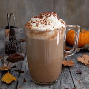 A glass with the latte inside and whipping cream and cocoa powder on top.