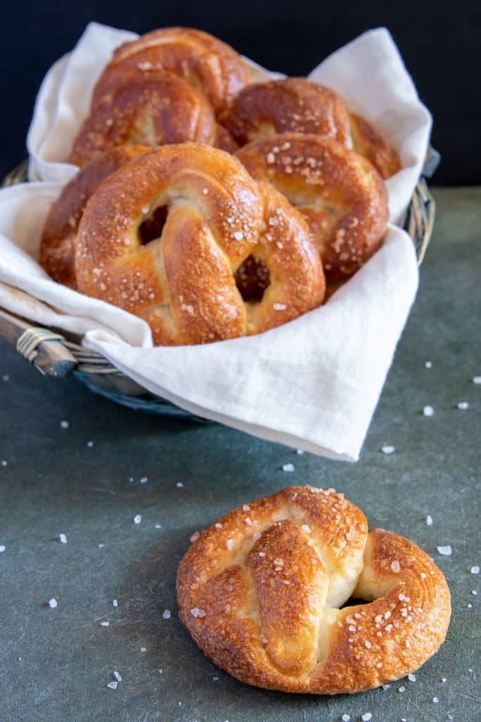 pretzels stuffed in a basket with a white cloth and one in front with some salt scattered around it.