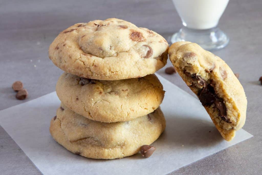 three cookies stacked and one leaning on the side with a glass of milk in the back.