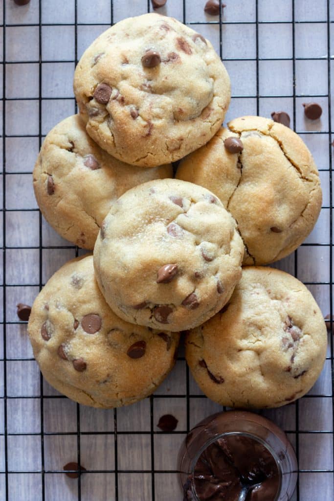 Cookies on top of a cooling rack with chocolate chips scattered around and a small jar of chocolate cream.