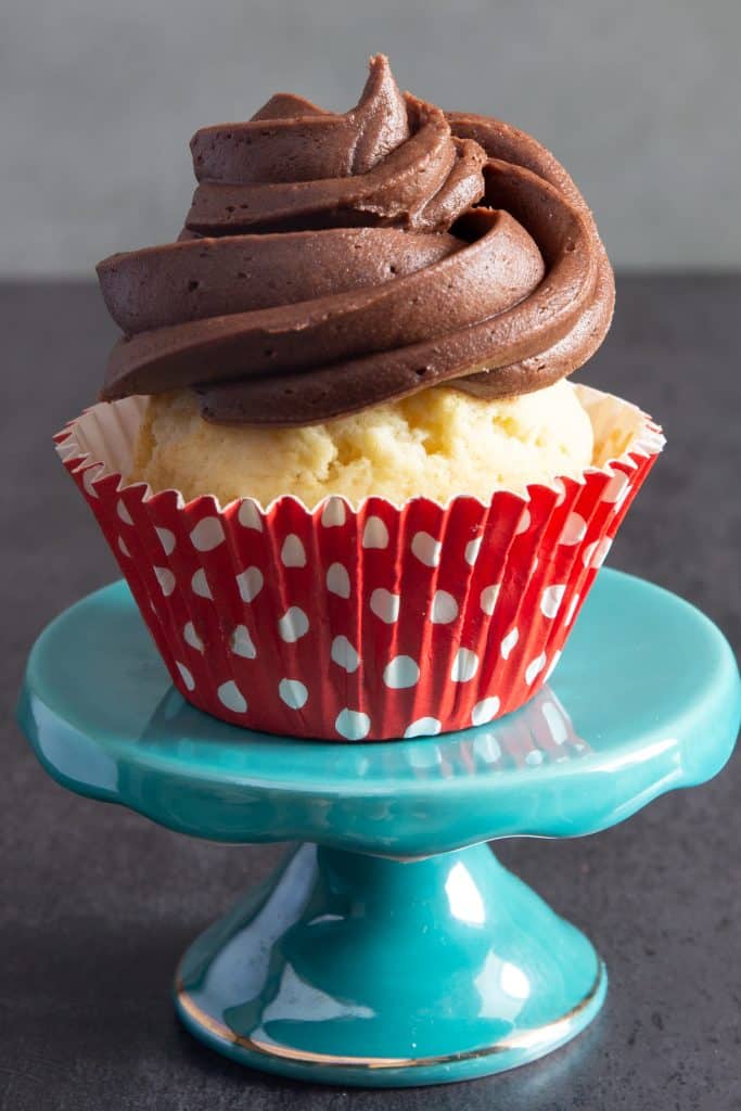 Cupcake with chocolate frosting on a small blue stand.