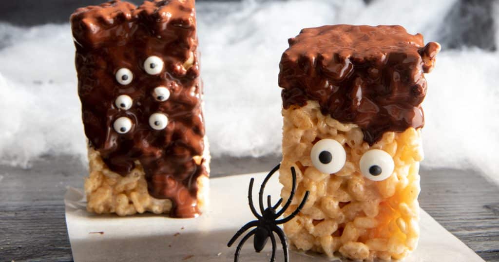 two halloween rice krispies squares with a fake spider crawling on one.