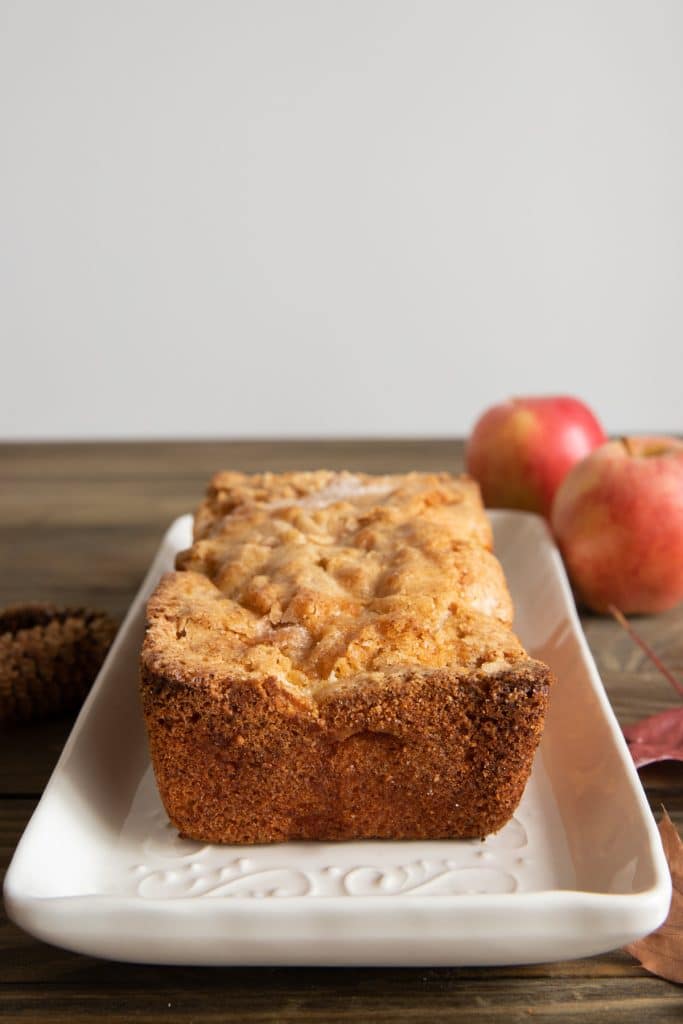 Cinnamon apple bread on a white plate with two apples in the back.