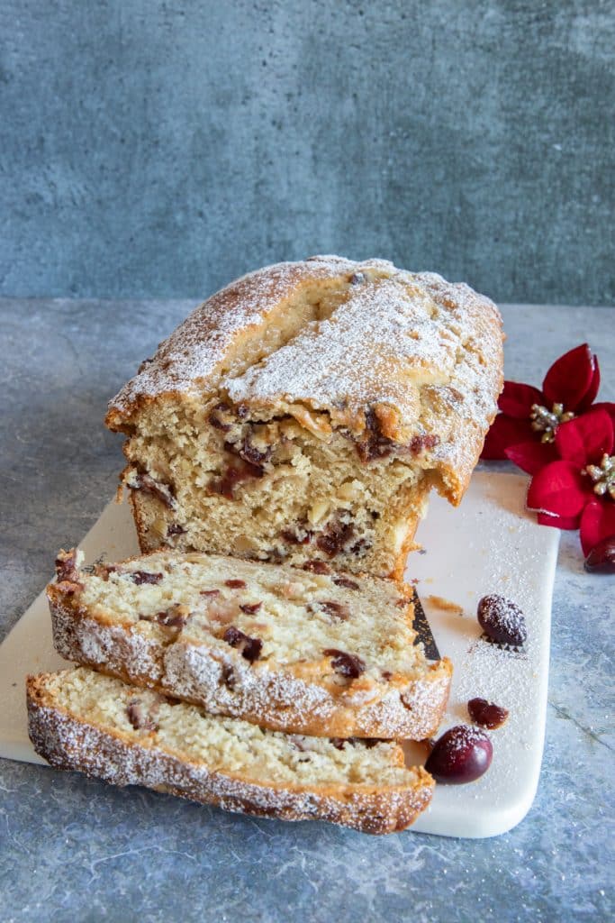 Cranberry bread on a white board with two slices in front.