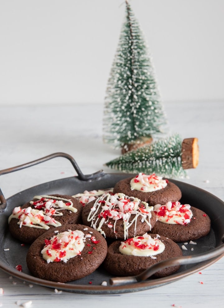 Peppermint cookies on a black plate with two christmas trees in the back.
