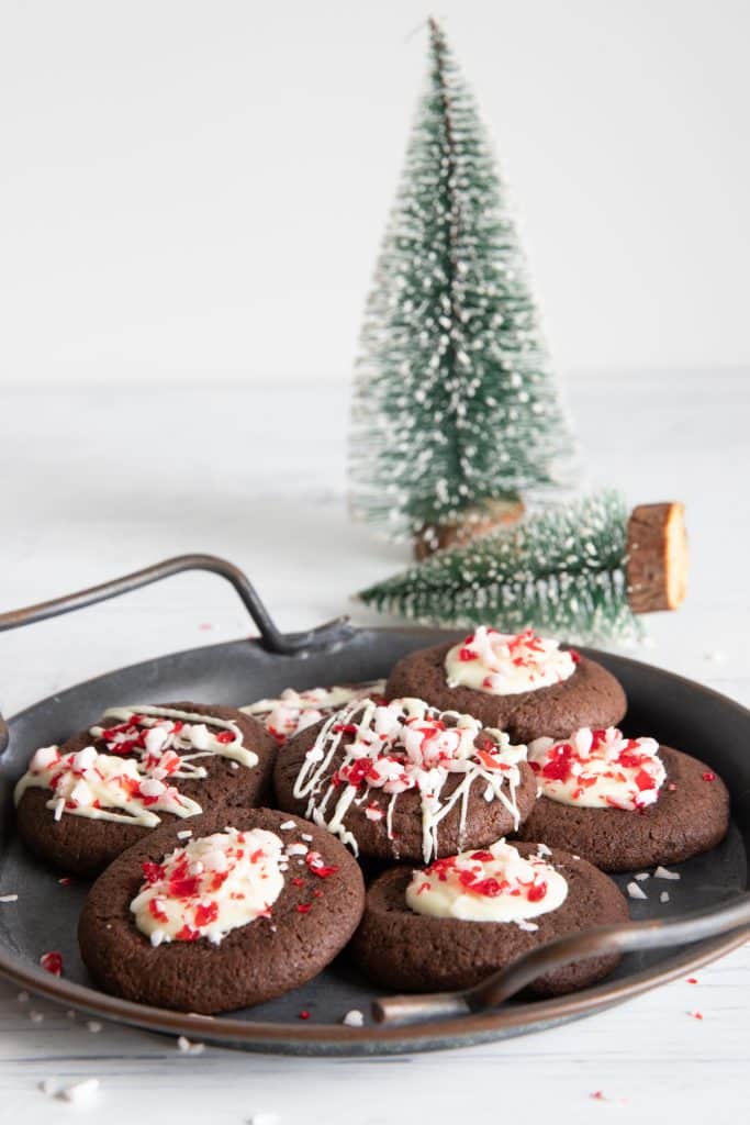 Chocolate cookies on a black plate with two Christmas trees in the back.