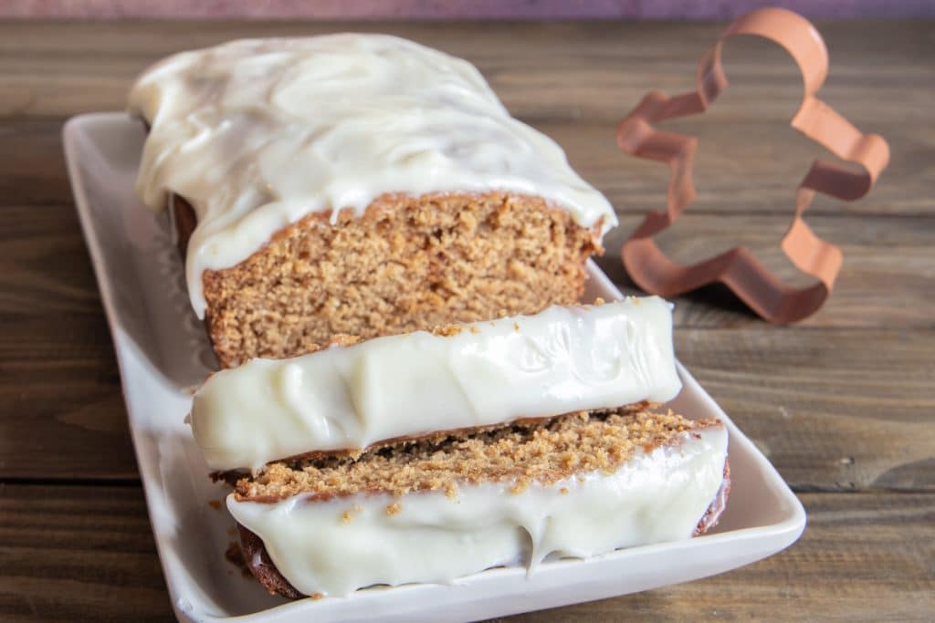 Gingerbread loaf with cream cheese frosting on a white board.