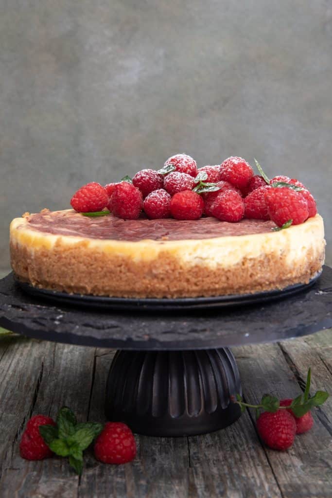 Cheesecake on a black cake stand with raspberries on top.