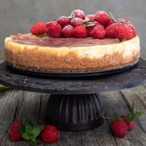 cake on a black cake stand with fresh raspberries on top.