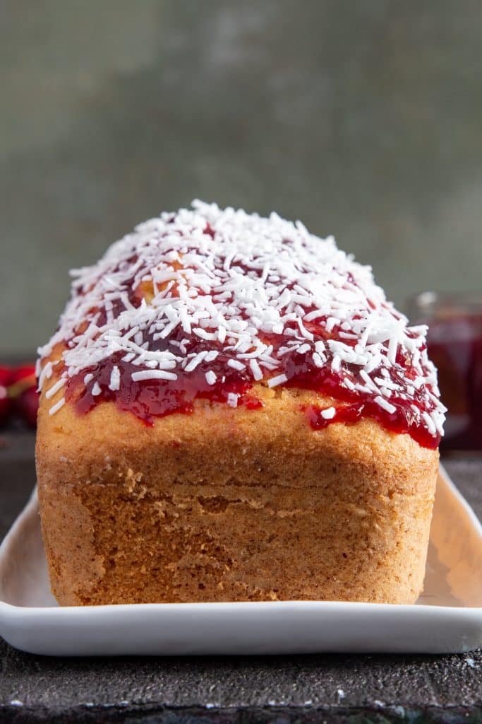 loaf on a white plate with cherry jam and shredded coconut on top.