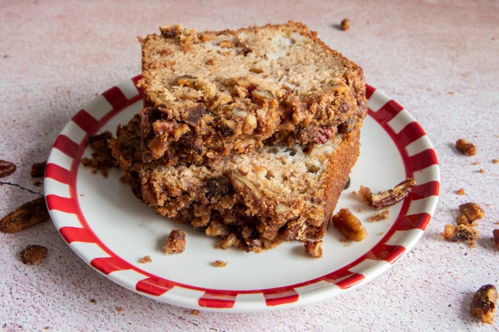 Two slices of apple pie bread on a white and red plate with chopped pecans scattered around.