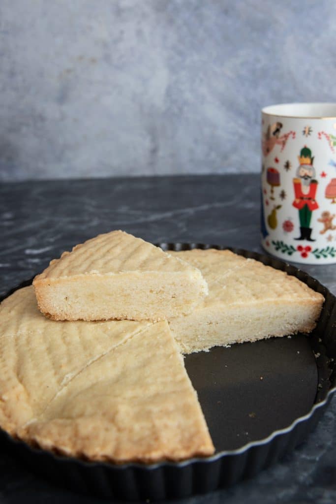 Shortbread slice on top of a black pan with cookies in it and a mug in the background.