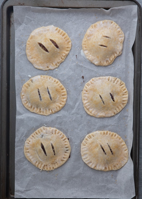 Hand pies sealed on a parchment paper lined cookie sheet.