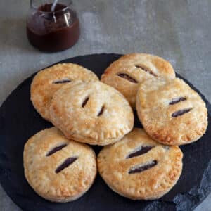 Six hand pies on a black plate with a jar of chocolate in the back.