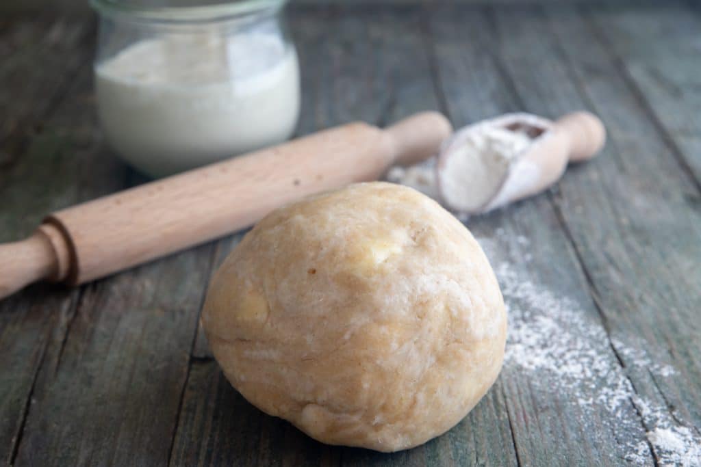 Pie dough on a board with a wooden rolling pin and sourdough starter.