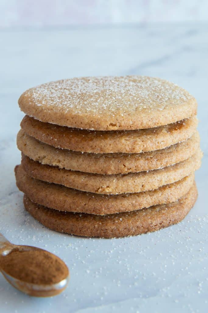 6 cookies stacked on top of each other with a teaspoon of cinnamon on the left side.