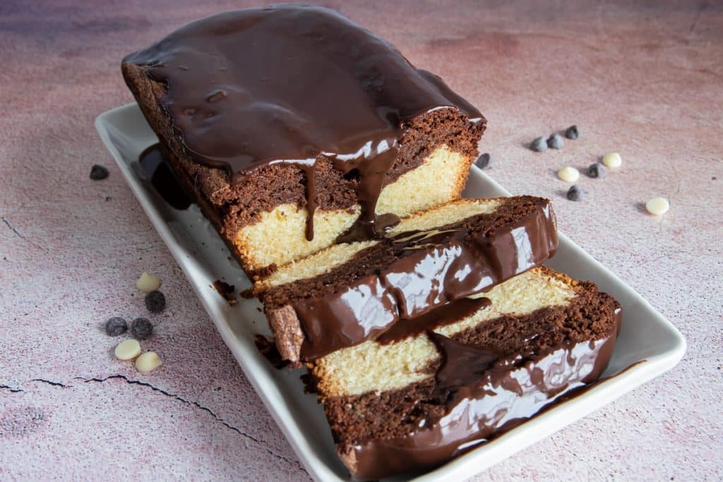 Two slices of marble pound cake and the rest of the cake on a white rectangular plate.