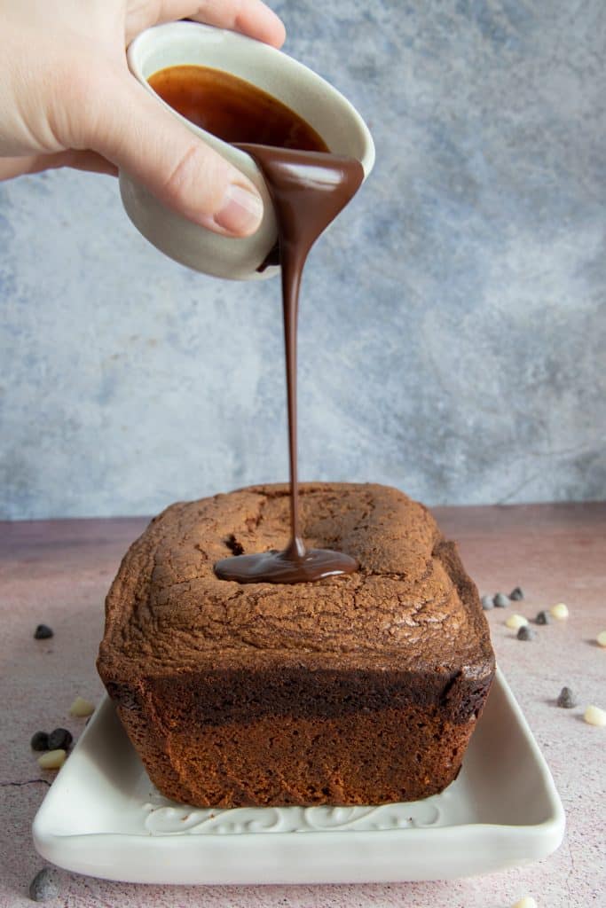 Pound cake with a hand pouring chocolate glaze on it.