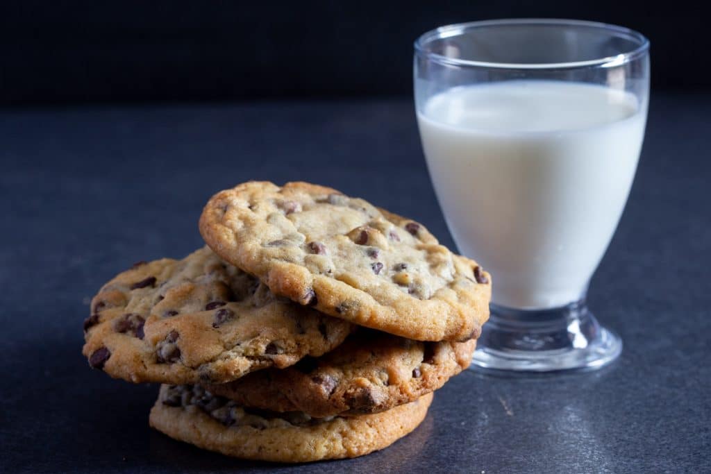 Four chocolate cookies one on top of the other and a glass of milk in the back.