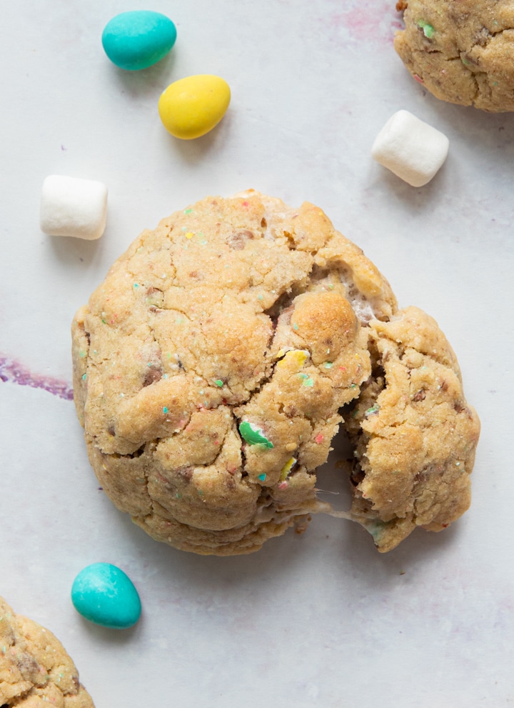 A broken cookie with marshmallows and mini eggs around it.