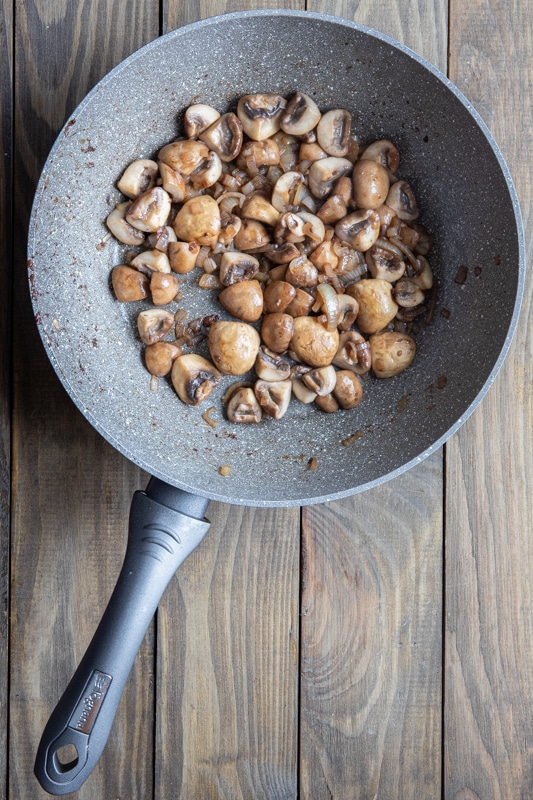 Cooked mushrooms and shallots in a pan.