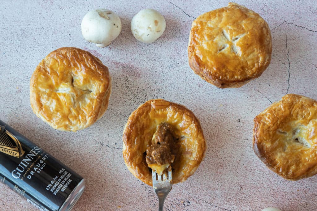 Four mini pies with a can of Guinness laying down and two mushrooms.