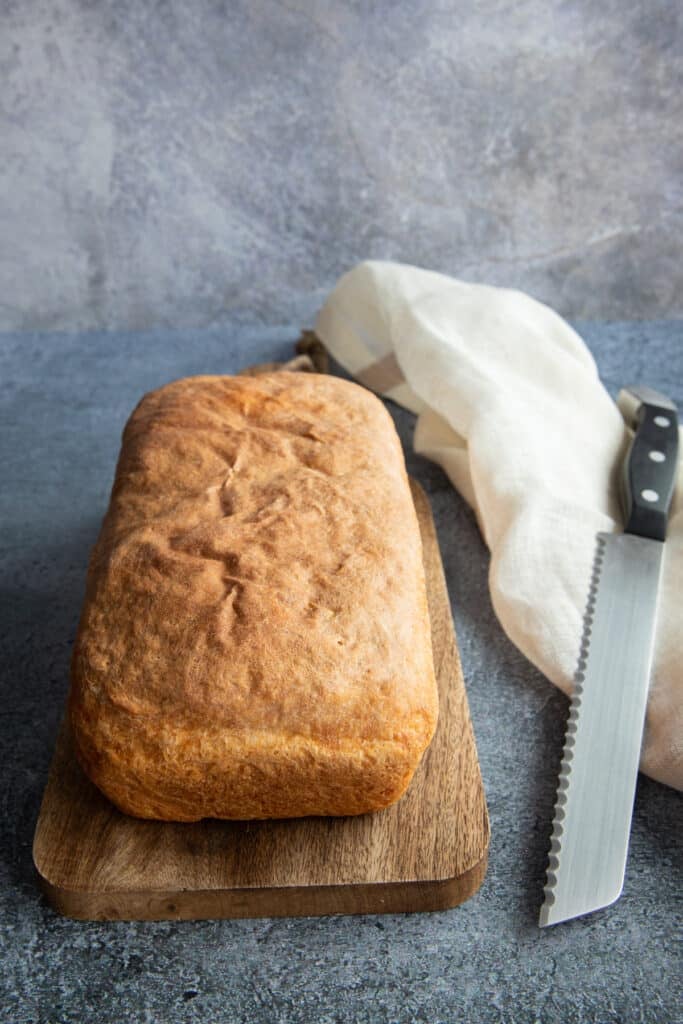 A loaf of buttermilk bread on a wooden board with a cloth and a bread knife on the right side.