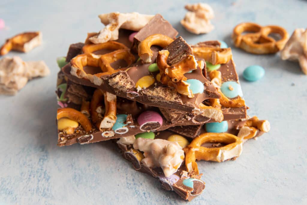 Three pieces of easter chocolate bark on top of each other with pretzels and smarties scattered around.