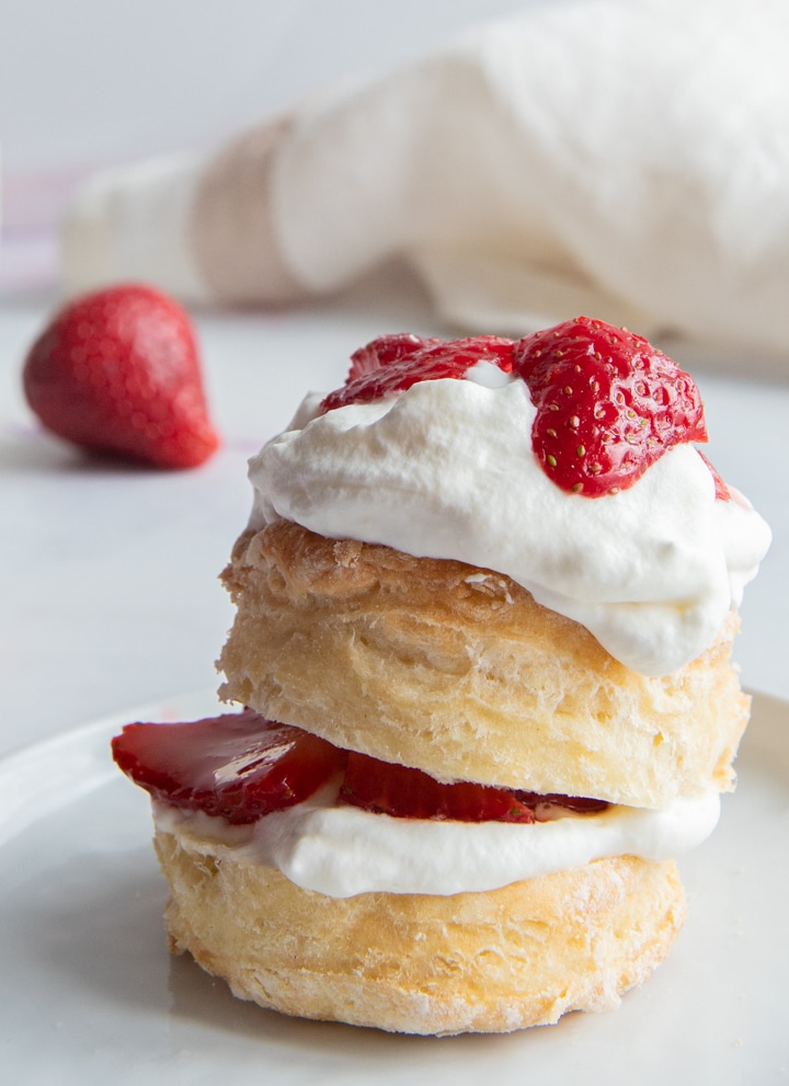 Shortcake biscuits topped with whipping cream and sliced strawberries on a white plate.