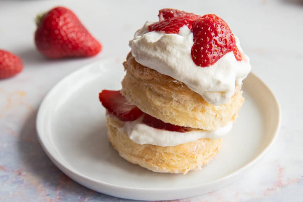 Strawberry shortcake biscuit on a white plate with two whole strawberries in the back.
