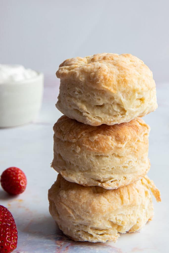 Three shortcake biscuits stacked on top of each other with whipping cream in a bowl in the back.