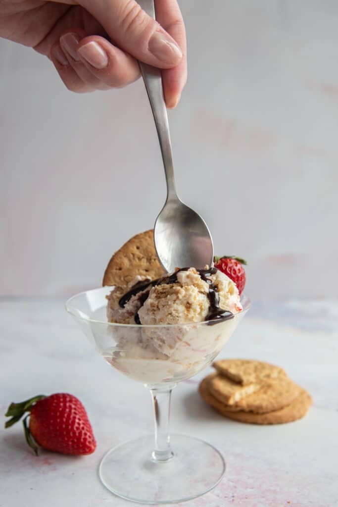 A hand holding a spoon over the ice cream in a glass.
