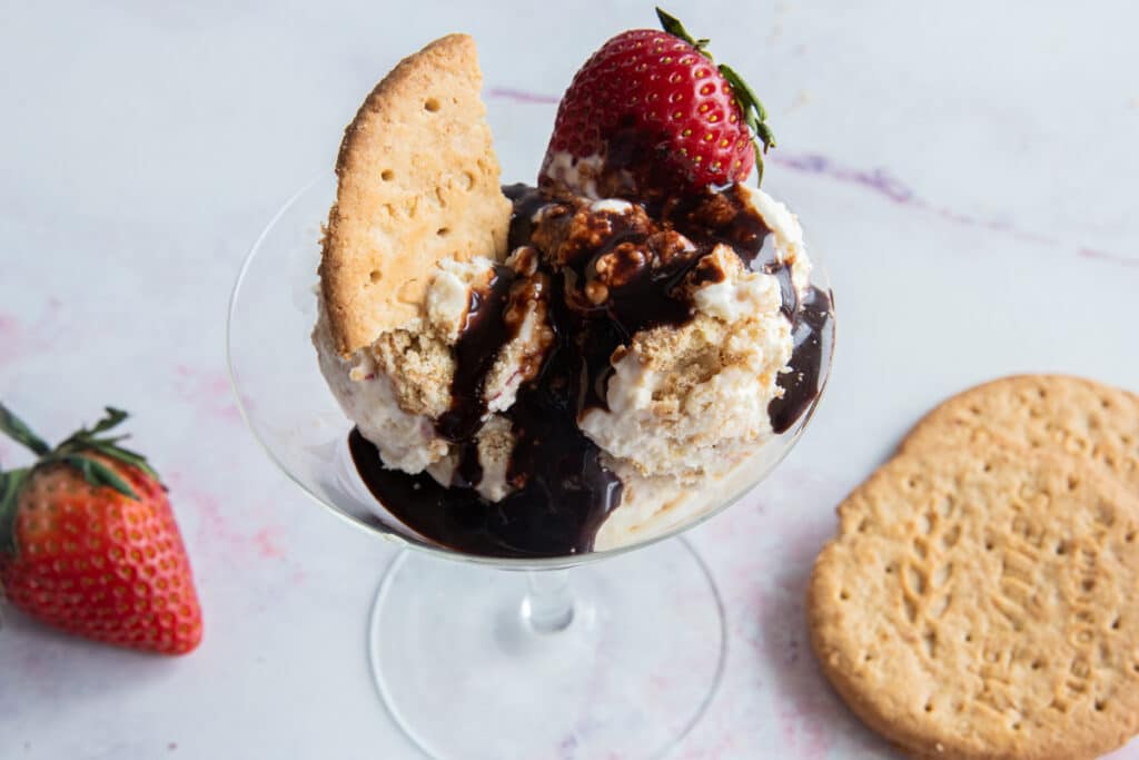 Ice cream in a glass with chocolate sauce on top and a strawberry and cookie as toppings.