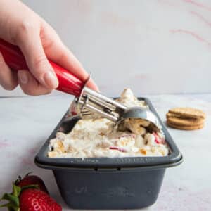 No churn ice cream in a loaf pan with a hand holding an ice cream scoop over it.