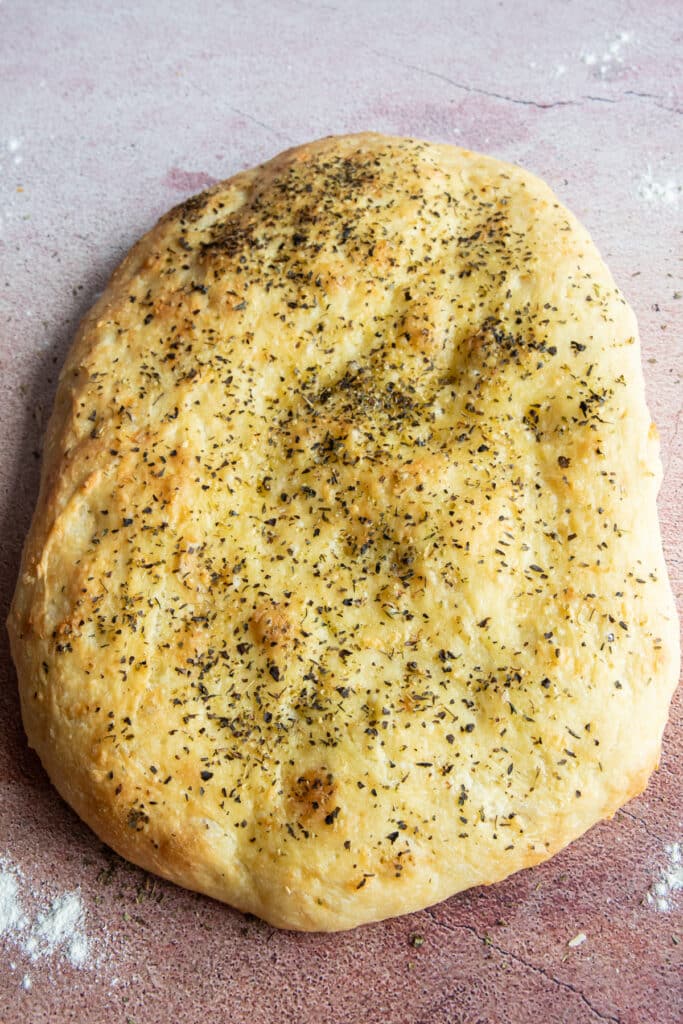 A whole focaccia with some flour sprinkled around it.