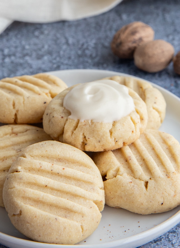 Five nutmeg cookies on a white plate with two nutmegs on the top right side of the photo.