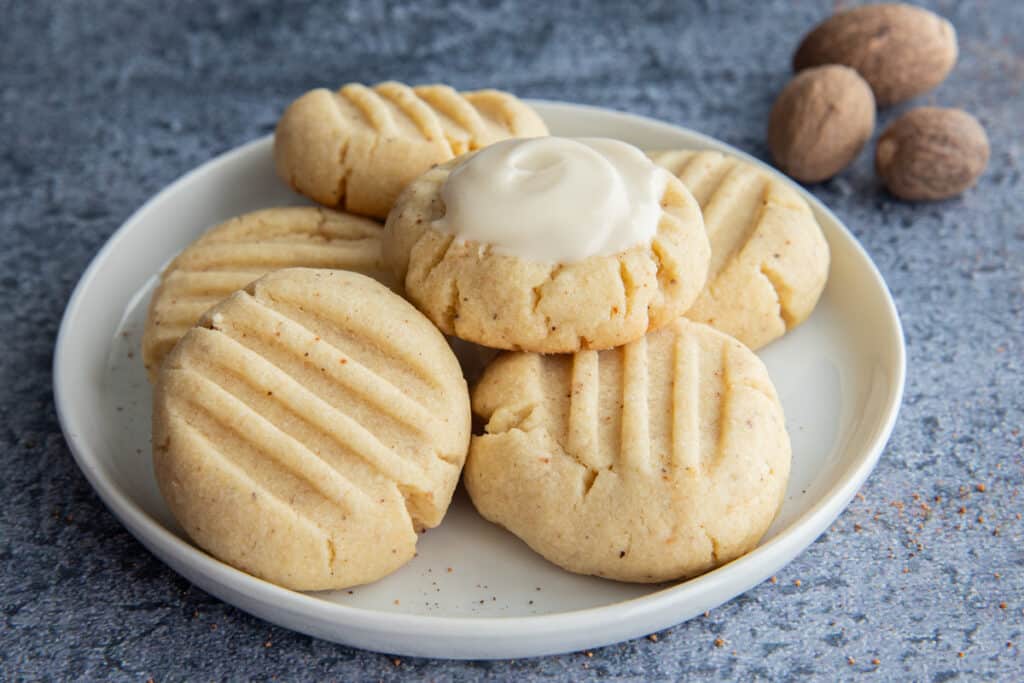 Cookies on a white plate with three nutmegs on the top right side of the photo.
