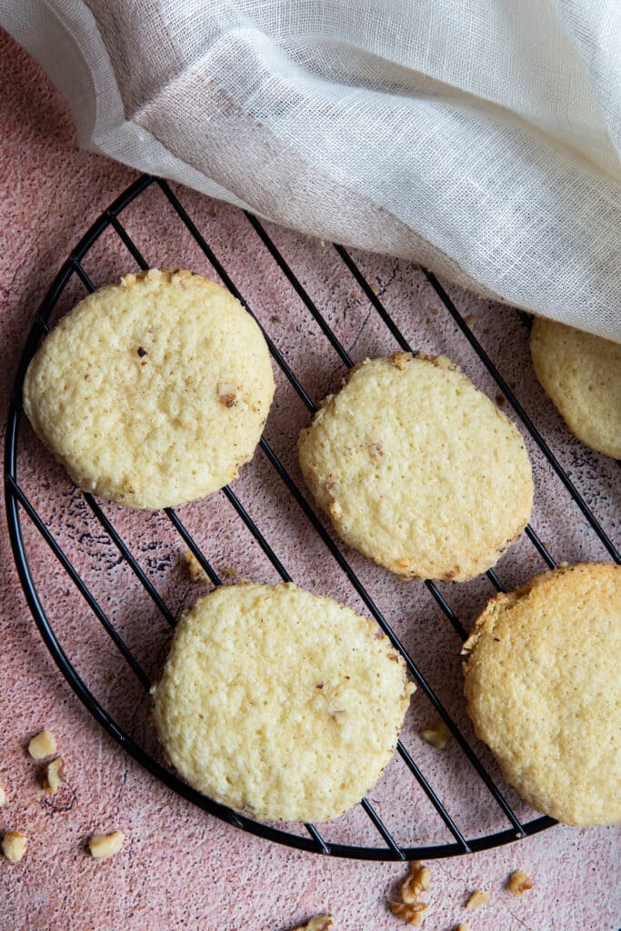 Five cookies on a black cooling rack with a white cloth on the top of the photo covering one of the cookies.