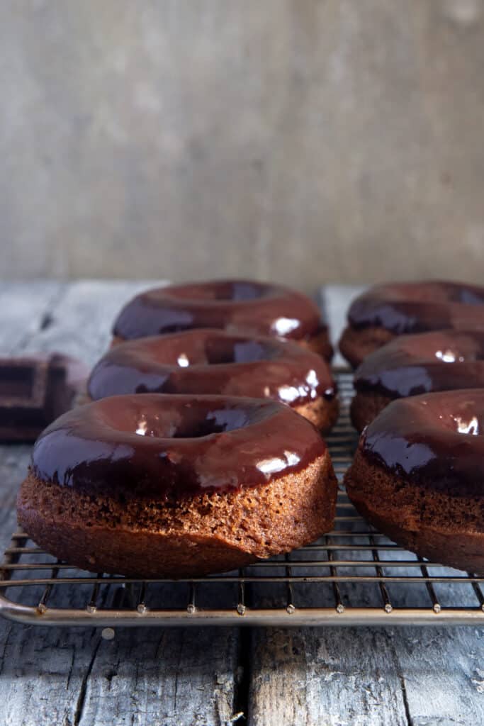 Six chocolate donuts on a cooling rack.
