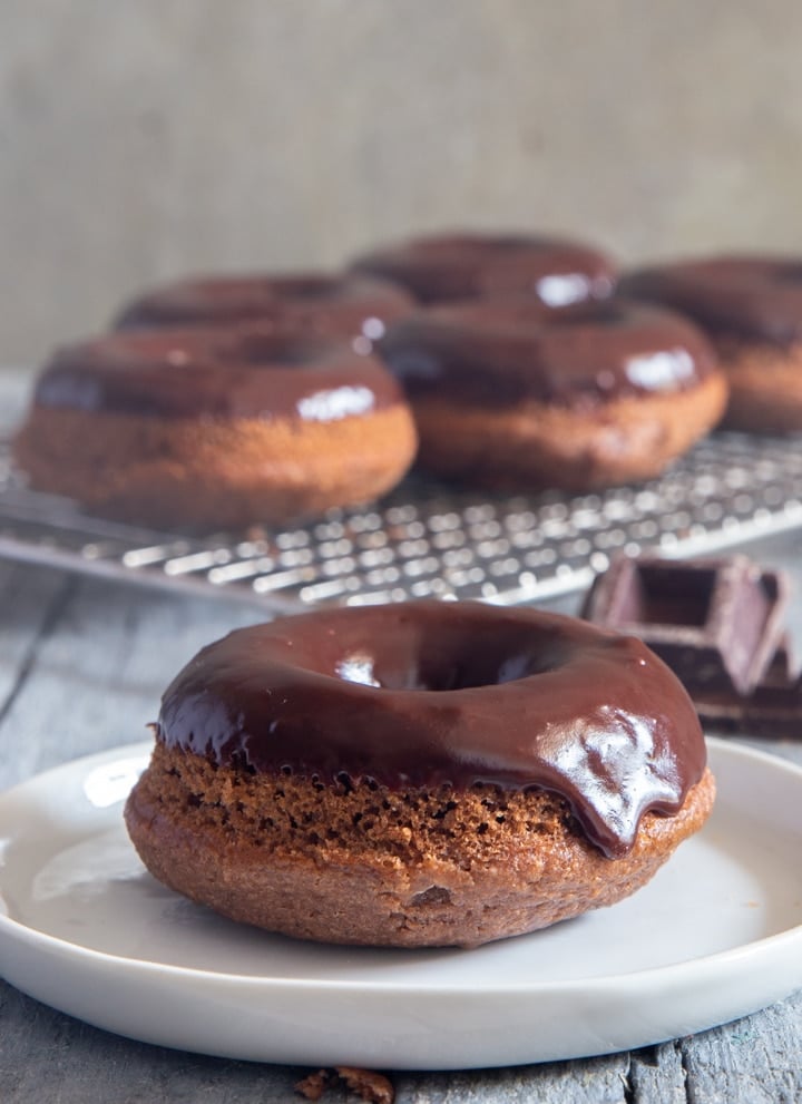 Donuts with a chocolate glaze on a wire rack and one on a plate.