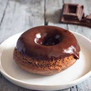 A chocolate glazed donut on a white plate.
