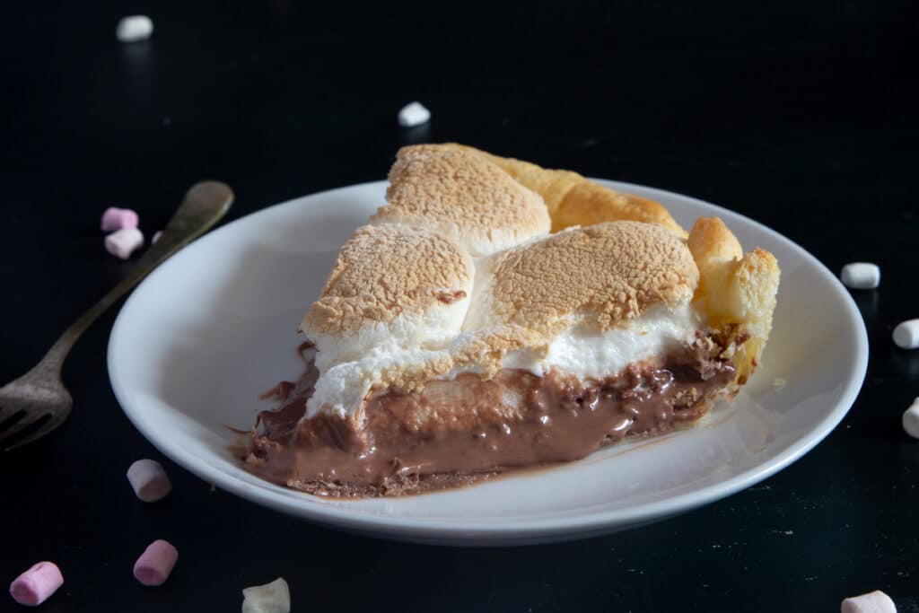 A slice of s'mores pie on a white plate with mini marshmallows around it.