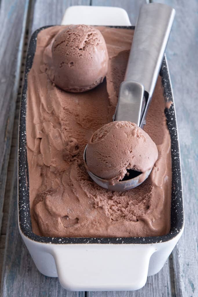 A loaf pan with chocolate frozen yogurt in it and two scoops on top with an ice cream scoop.