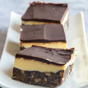 Three nanaimo bars lined in front of one another on a white plate.