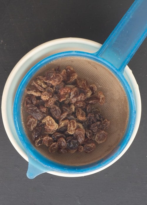 Soaked raisins in a sieve on top of a bowl.