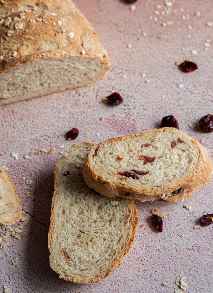 Two slices od oats and cranberry bread with dried cranberries scattered around.