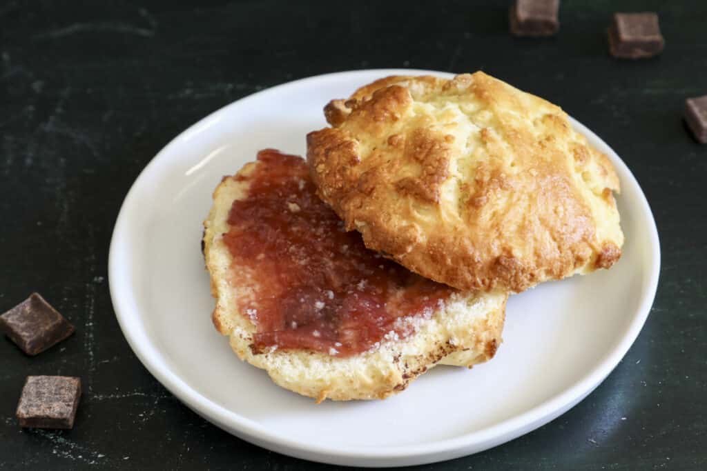 A cut chocolate chip scone with jam in the middle on a white plate.